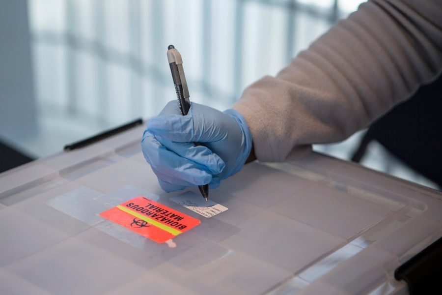 A University COVID-19 testing site worker writes on a box containing completed COVID-19 tests on Oct. 9.